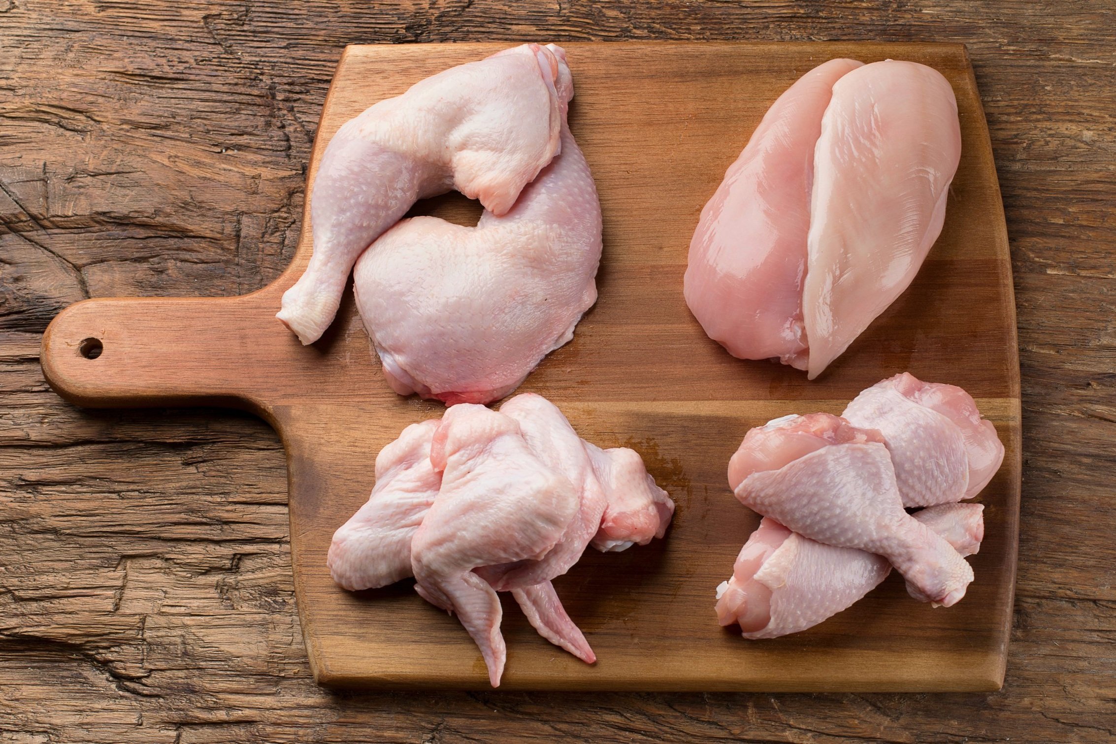 Raw chicken pieces including drumsticks, thighs, and breasts arranged on a wooden cutting board, showcasing different cuts for cooking and meal preparation.